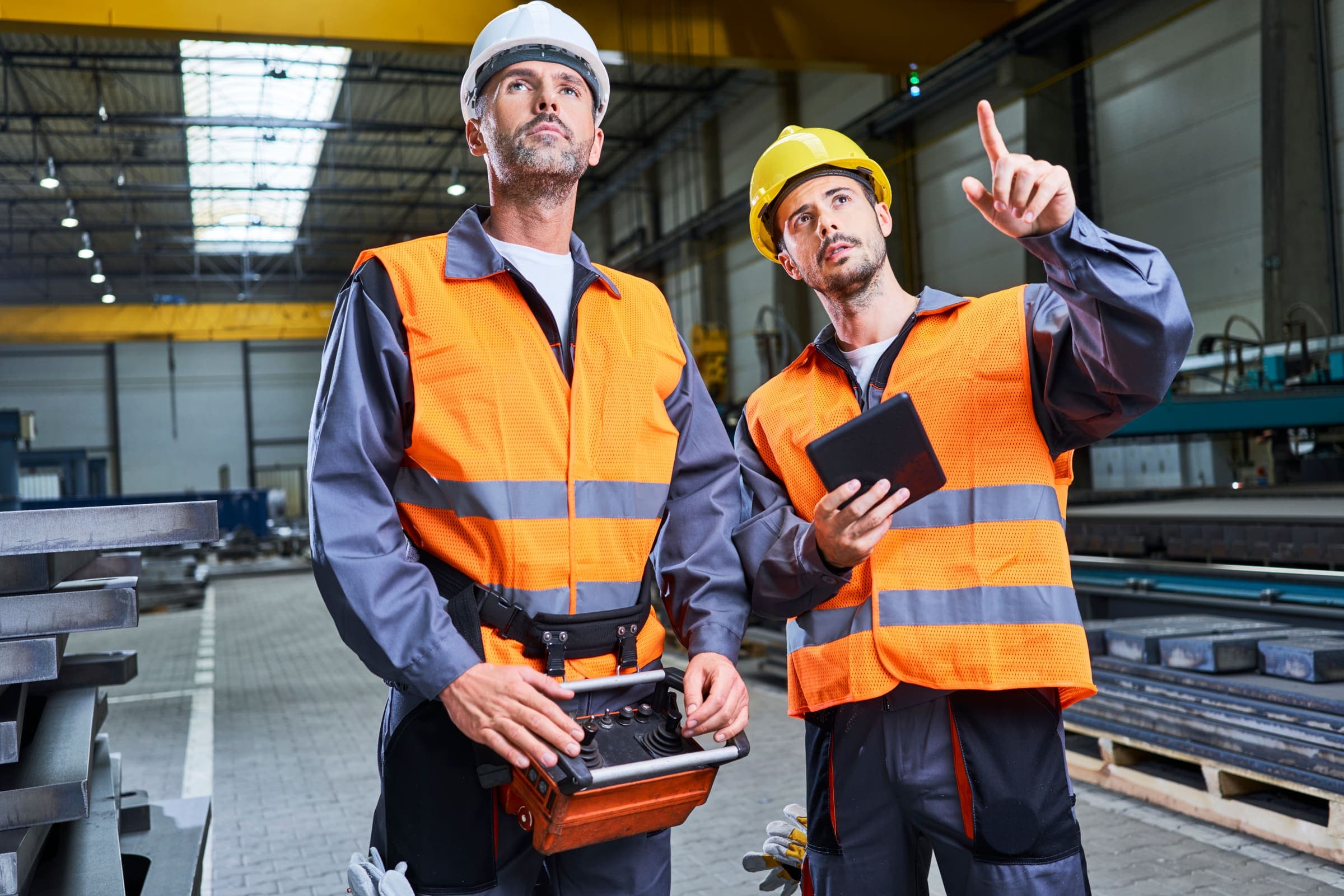 Factory workers inspecting overhead crane equipment using a tablet